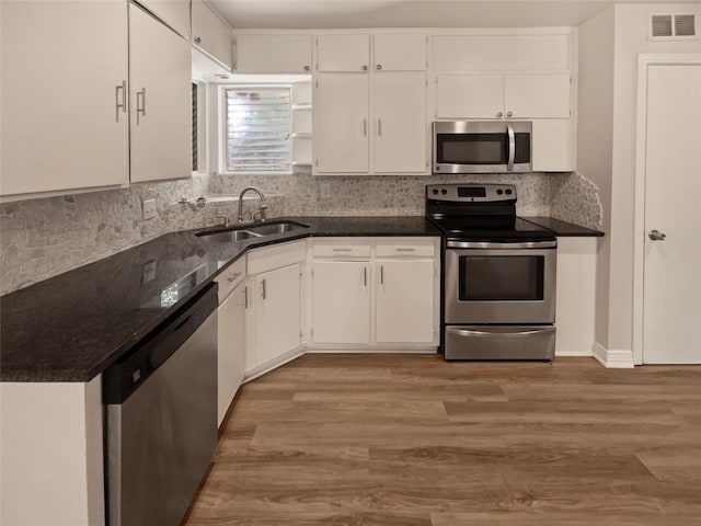 kitchen featuring white cabinets, dark stone countertops, light wood-type flooring, sink, and stainless steel appliances