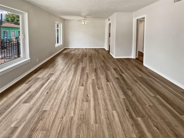 unfurnished room with ceiling fan, a wealth of natural light, dark wood-type flooring, and a textured ceiling