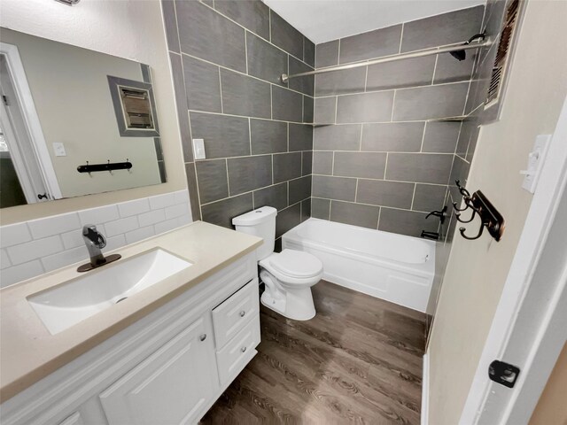 full bathroom featuring toilet, wood-type flooring, vanity, tiled shower / bath combo, and decorative backsplash