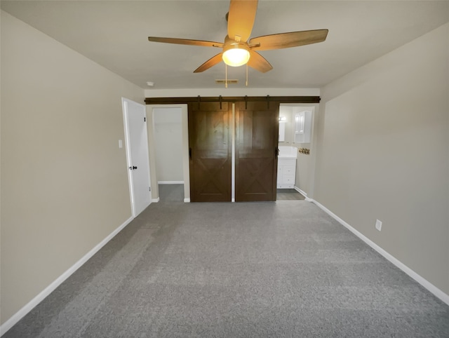 unfurnished bedroom with a barn door, ceiling fan, and dark carpet