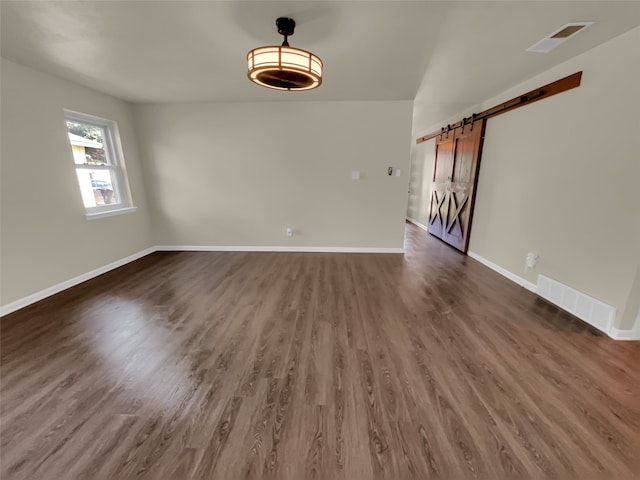 empty room with a barn door and dark hardwood / wood-style flooring