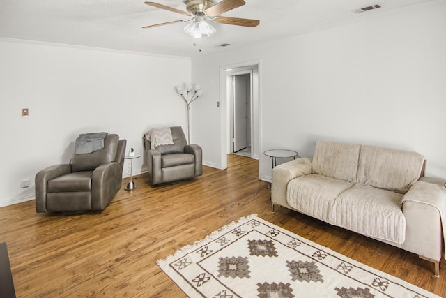 living area featuring visible vents, a ceiling fan, wood finished floors, crown molding, and baseboards