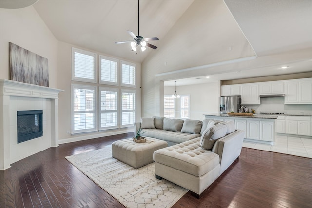 living room with ceiling fan with notable chandelier, dark hardwood / wood-style flooring, a towering ceiling, and a tiled fireplace