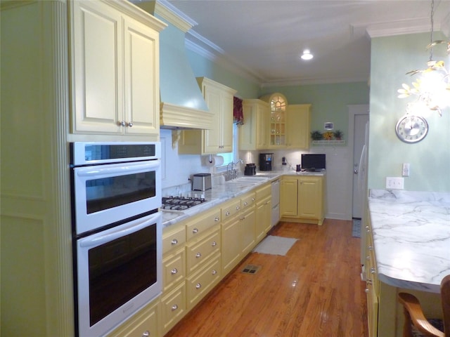 kitchen with light stone countertops, white appliances, wall chimney range hood, sink, and ornamental molding