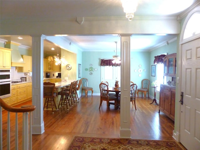 dining room with crown molding, hardwood / wood-style flooring, an inviting chandelier, and decorative columns