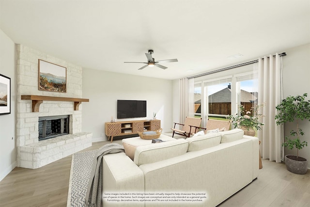 living room featuring light hardwood / wood-style floors, a stone fireplace, and ceiling fan