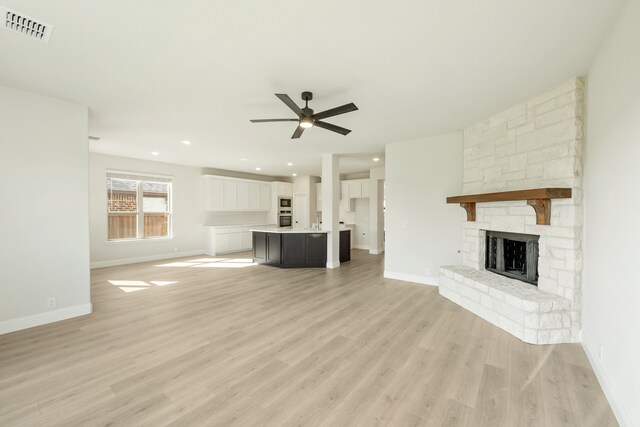 unfurnished living room with ceiling fan, a stone fireplace, and light wood-type flooring