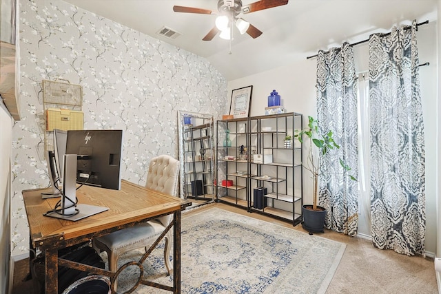 carpeted home office with wallpapered walls, visible vents, a ceiling fan, and lofted ceiling