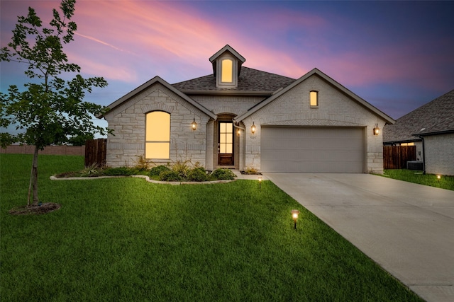 french country inspired facade with a garage, driveway, a shingled roof, and a lawn