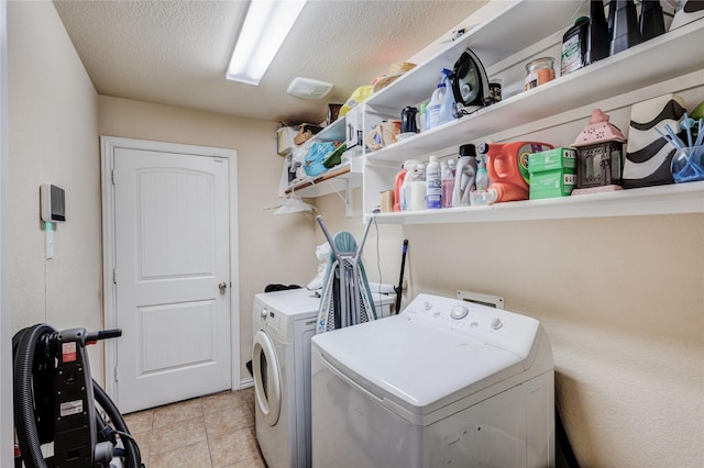 clothes washing area featuring washing machine and clothes dryer, light tile patterned flooring, and a textured ceiling