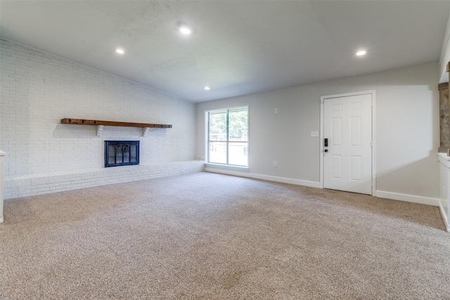 unfurnished living room with carpet flooring, a brick fireplace, and brick wall