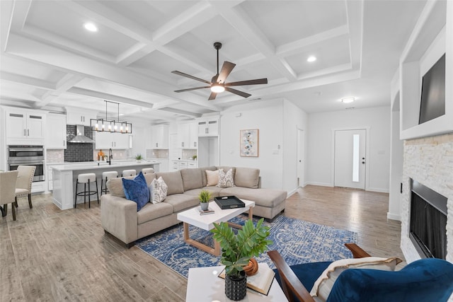 living room with coffered ceiling, ceiling fan, beam ceiling, light hardwood / wood-style flooring, and a fireplace