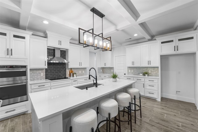 kitchen featuring white cabinetry, sink, wall chimney range hood, and a center island with sink