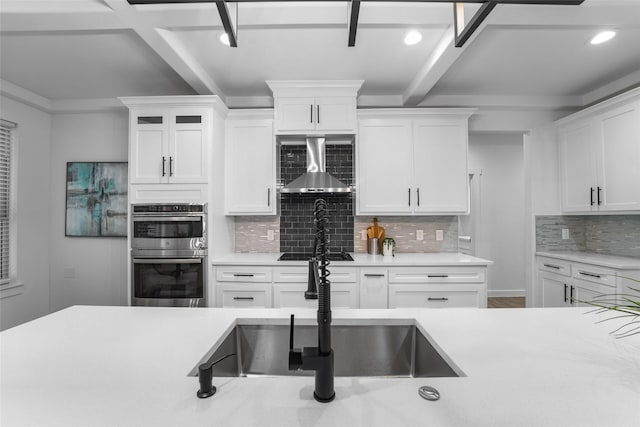 kitchen with wall chimney exhaust hood, stainless steel double oven, sink, beam ceiling, and white cabinets