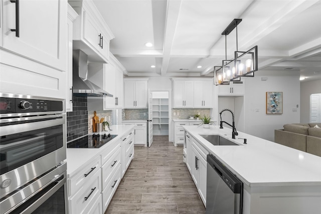 kitchen featuring sink, an island with sink, appliances with stainless steel finishes, beam ceiling, and extractor fan