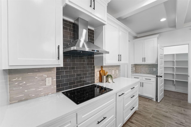 kitchen featuring white cabinets, backsplash, black electric cooktop, and wall chimney exhaust hood