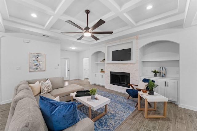 living room with ceiling fan, built in features, a fireplace, and coffered ceiling