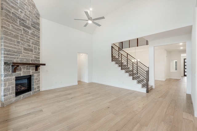 unfurnished living room featuring ceiling fan, high vaulted ceiling, a stone fireplace, and light hardwood / wood-style floors