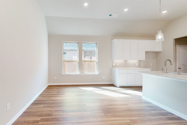 kitchen featuring sink, hanging light fixtures, white cabinets, decorative backsplash, and light hardwood / wood-style flooring