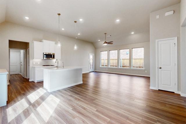 kitchen with light wood-type flooring, white cabinetry, vaulted ceiling, decorative light fixtures, and a center island with sink