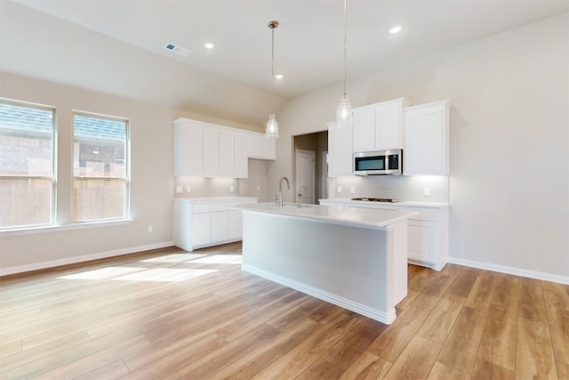 kitchen with sink, light wood-type flooring, an island with sink, white cabinetry, and pendant lighting