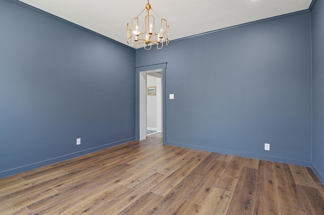 empty room featuring hardwood / wood-style flooring, an inviting chandelier, and crown molding