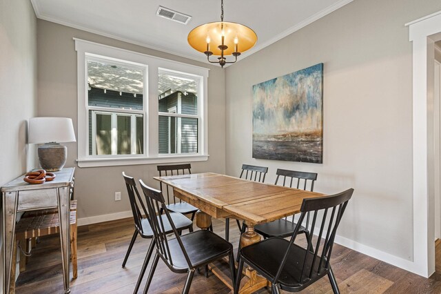 dining space with hardwood / wood-style flooring, ornamental molding, and an inviting chandelier