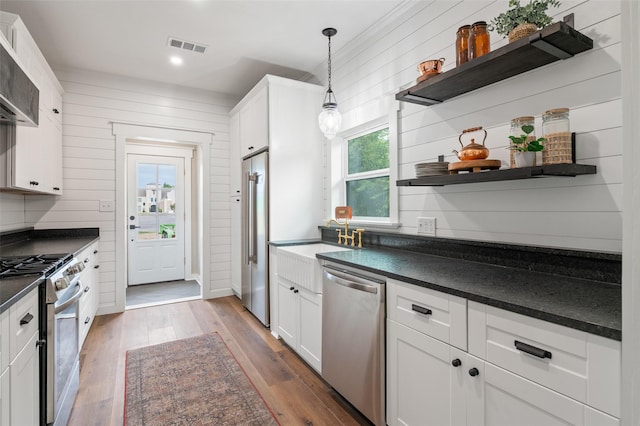 kitchen featuring wood walls, light hardwood / wood-style floors, decorative light fixtures, high quality appliances, and white cabinets