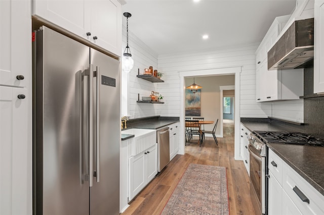 kitchen with white cabinetry, wall chimney exhaust hood, premium appliances, decorative light fixtures, and hardwood / wood-style flooring