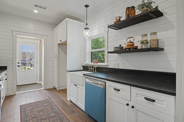 kitchen featuring white cabinets, stainless steel dishwasher, and wood walls