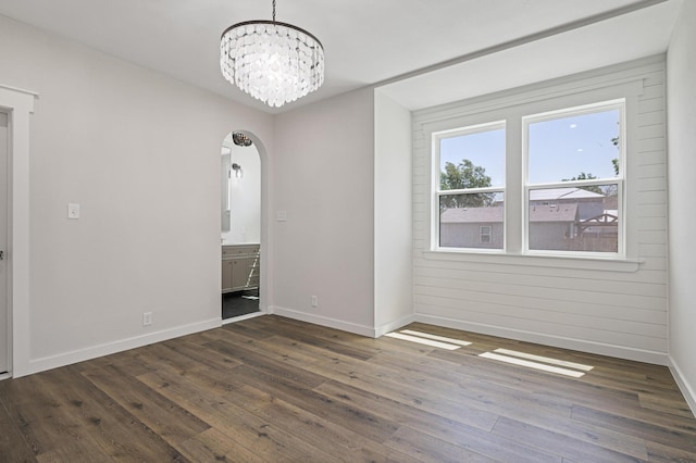 spare room with a notable chandelier, dark hardwood / wood-style flooring, and wooden walls