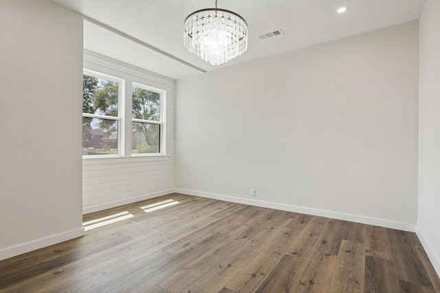 empty room featuring wood-type flooring and an inviting chandelier