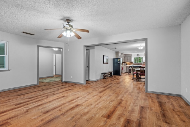 unfurnished living room with a textured ceiling, light hardwood / wood-style flooring, and ceiling fan