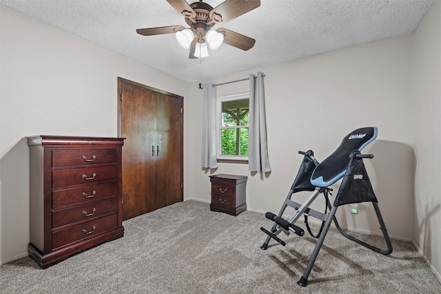 exercise room with a textured ceiling, light colored carpet, and ceiling fan