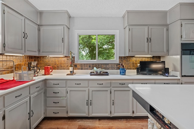 kitchen with light wood-type flooring, a textured ceiling, wall oven, and backsplash