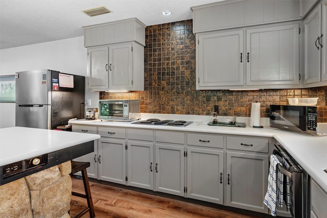 kitchen with gray cabinetry, beverage cooler, white gas cooktop, stainless steel fridge, and light wood-type flooring