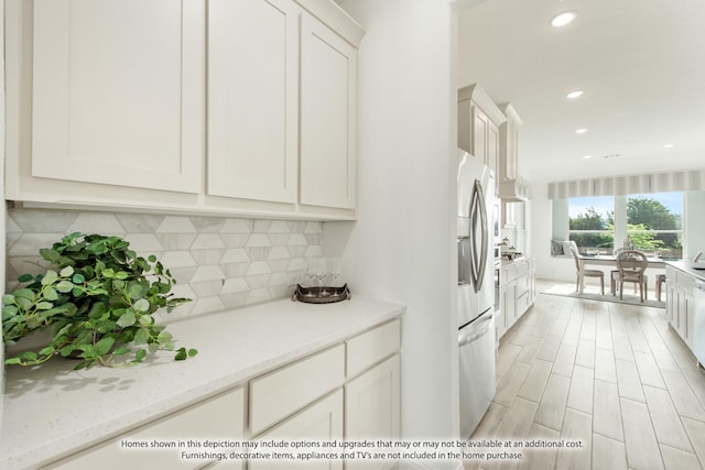 kitchen featuring light stone countertops, stainless steel fridge, backsplash, light hardwood / wood-style flooring, and white cabinets