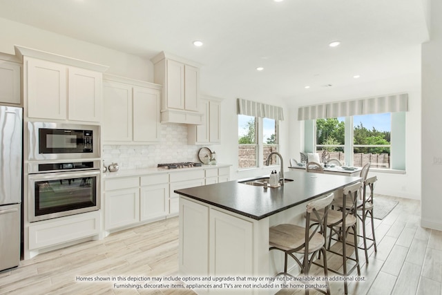 kitchen with a wealth of natural light, sink, stainless steel appliances, a center island with sink, and white cabinets