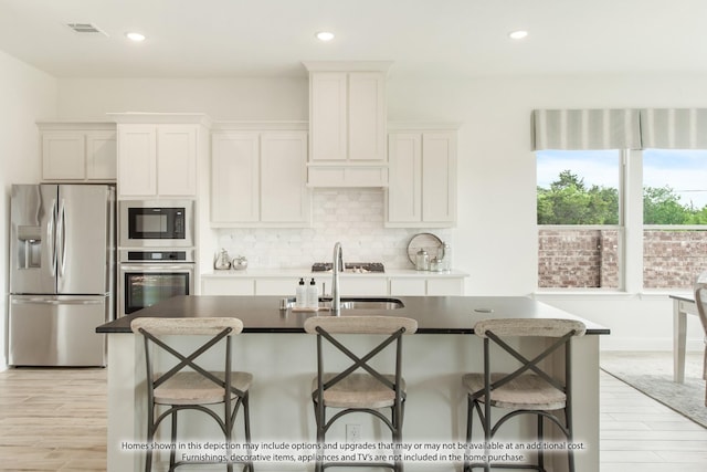 kitchen featuring white cabinets, a kitchen breakfast bar, a center island with sink, and stainless steel appliances