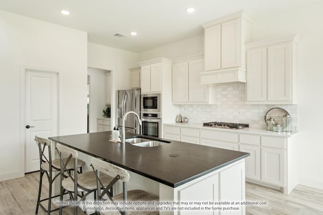 kitchen with a kitchen island with sink, sink, appliances with stainless steel finishes, light hardwood / wood-style floors, and white cabinetry