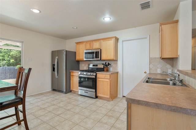 kitchen featuring appliances with stainless steel finishes, light brown cabinetry, sink, backsplash, and light tile patterned floors