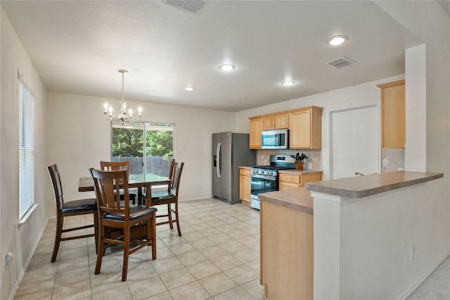 kitchen with light brown cabinetry, tasteful backsplash, a chandelier, kitchen peninsula, and stainless steel appliances