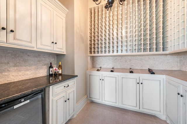 kitchen with tasteful backsplash, white cabinetry, dishwasher, dark stone counters, and light tile patterned floors