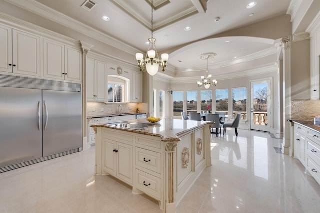 kitchen with built in refrigerator, a center island, a chandelier, a tray ceiling, and pendant lighting