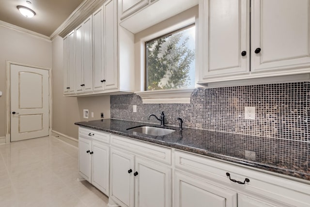 kitchen with white cabinetry, sink, backsplash, dark stone counters, and ornamental molding