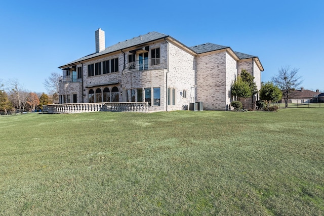 back of house featuring cooling unit, a balcony, and a yard