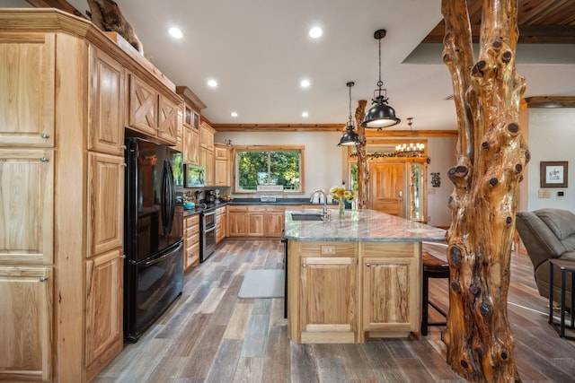 kitchen featuring dark wood-type flooring, an island with sink, light stone counters, black refrigerator, and sink