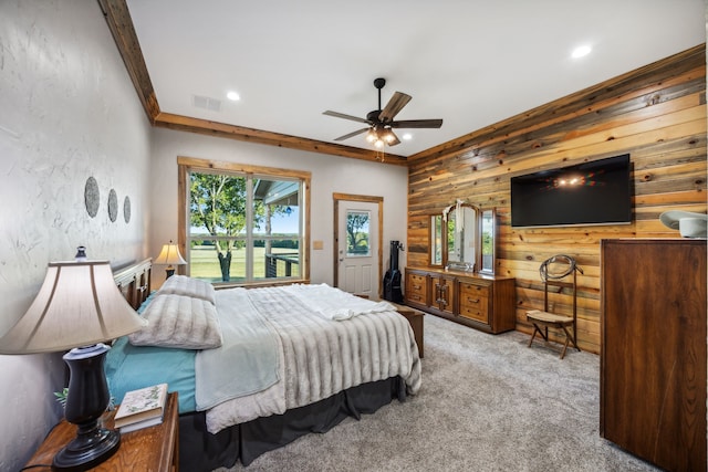 carpeted bedroom with ornamental molding, wood walls, and ceiling fan