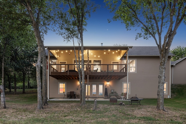 back house at dusk with french doors, a balcony, a lawn, and a patio area