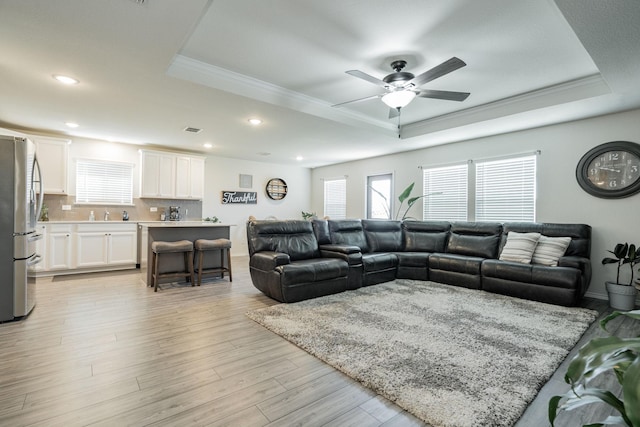 living room featuring a raised ceiling, crown molding, light hardwood / wood-style flooring, and ceiling fan